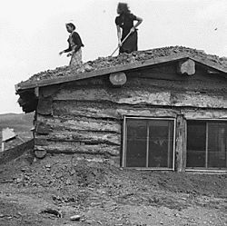 Women putting sod on a roof of a log cabin