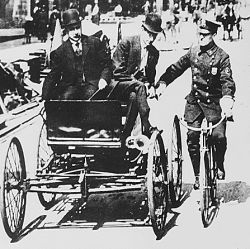 Traffic violator driving a 1900-vintage car being stopped by a policeman on a bicycle