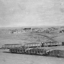 "Birds Eye View of Winslow, looking East." Atlantic and Pacific Railway cars on converging tracks in the foreground of the arid Arizona terrain