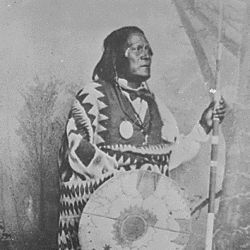 San Juan, a Mescalero Apache chief; standing, full-length, holding a spear and shield 