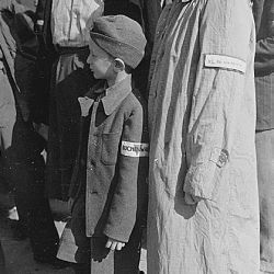 Six-year-old war orphan with Buchenwald badge on his sleeve waits for his name to be called at roll call at Buchenwald camp, Germany, for departure to Switzerland