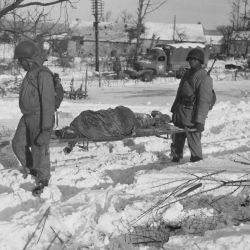 "Body of American soldier is borne on stretcher from terrain in vicinity of Malmedy, Belgium, where on or about 17 December 1944, the Germans committed many atrocities."