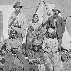 Winema or Tobey Riddle, a Modoc, standing between an agent and her husband Frank (on her left), with four Modoc women in front
