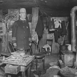 Two officials of the New York City Tenement House Department inspect a cluttered basement living room